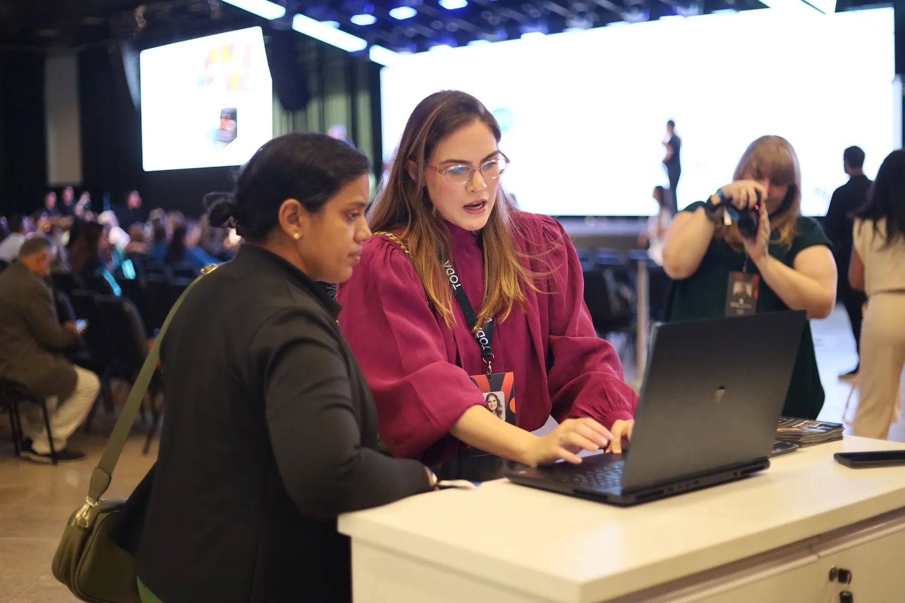 Profissionais conversam diante de um notebook no espaço de um evento