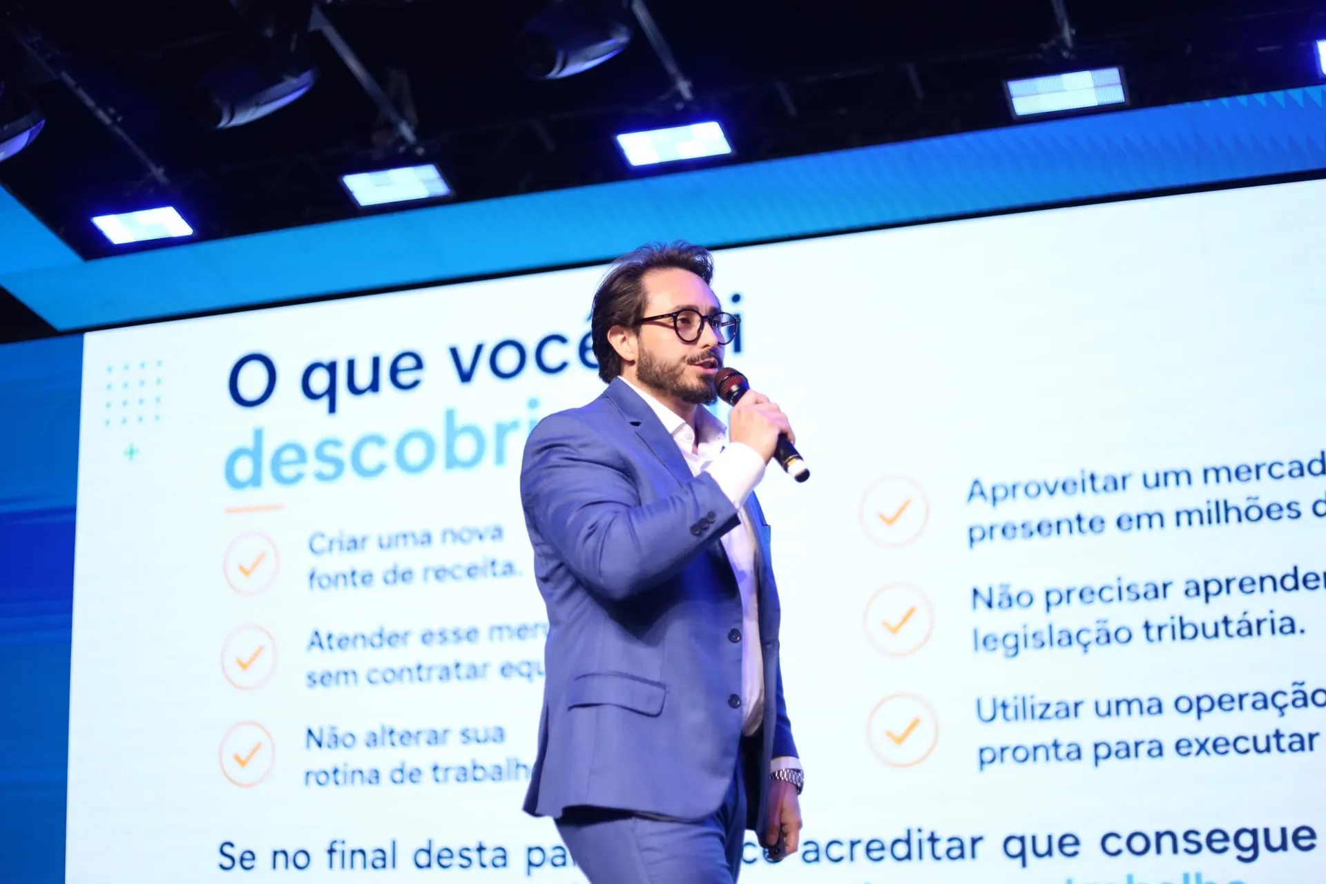 Kleber Toda fala ao microfone diante de uma apresentação projetada