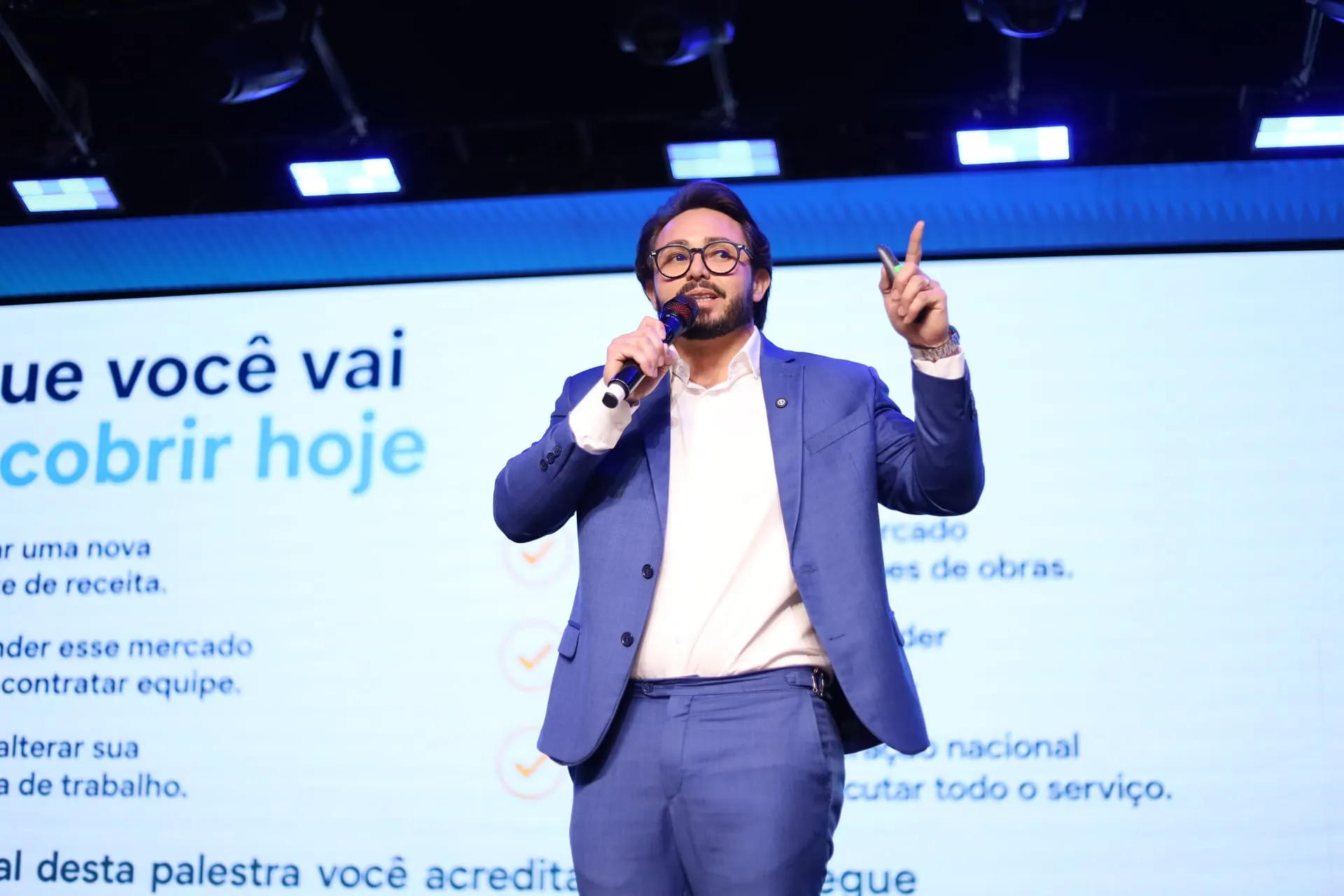 Kleber Toda fala ao microfone e aponta para cima durante uma apresentação