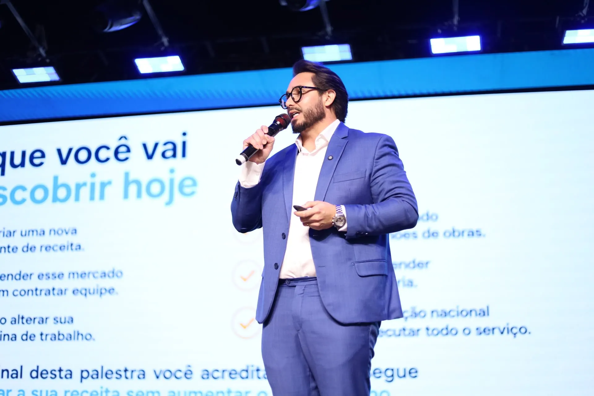 Kleber Toda fala ao microfone em um palco, visto de perfil